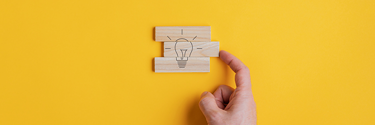 Wide view image of male hand assembling a light bulb drawing on wooden pegs in a conceptual image.