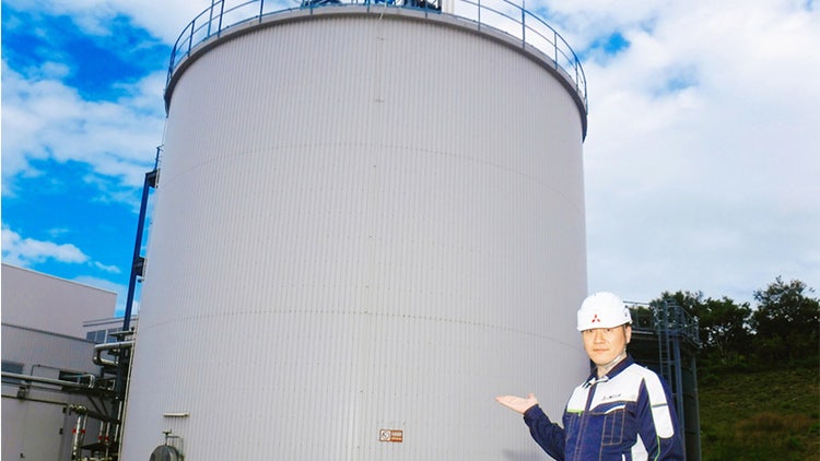 三菱化工機 稚内市バイオエネルギーセンター 所長の畑野慎二氏。同センターのメタン発酵槽を背景に