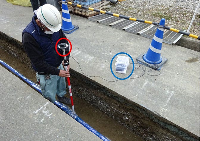 配水管工事の現場で、パイプを接合し地中に埋めていく際の位置情報記録の様子。 赤丸部分にアンテナ、青丸部分がGNSS受信機。